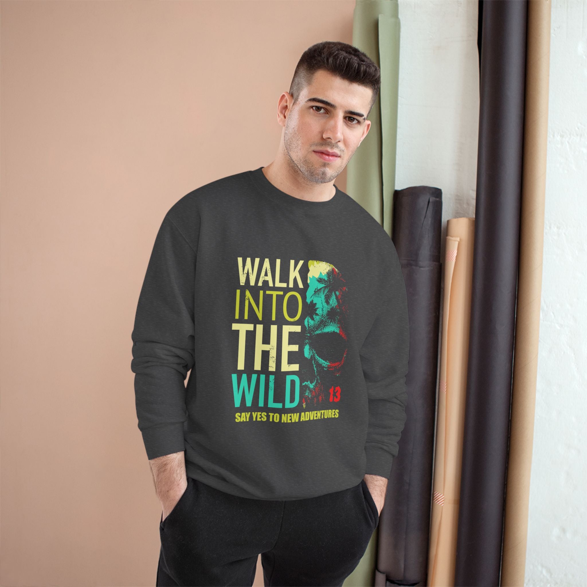 Man wearing a black sweatshirt with colorful text and graphic design, standing against a beige wall.