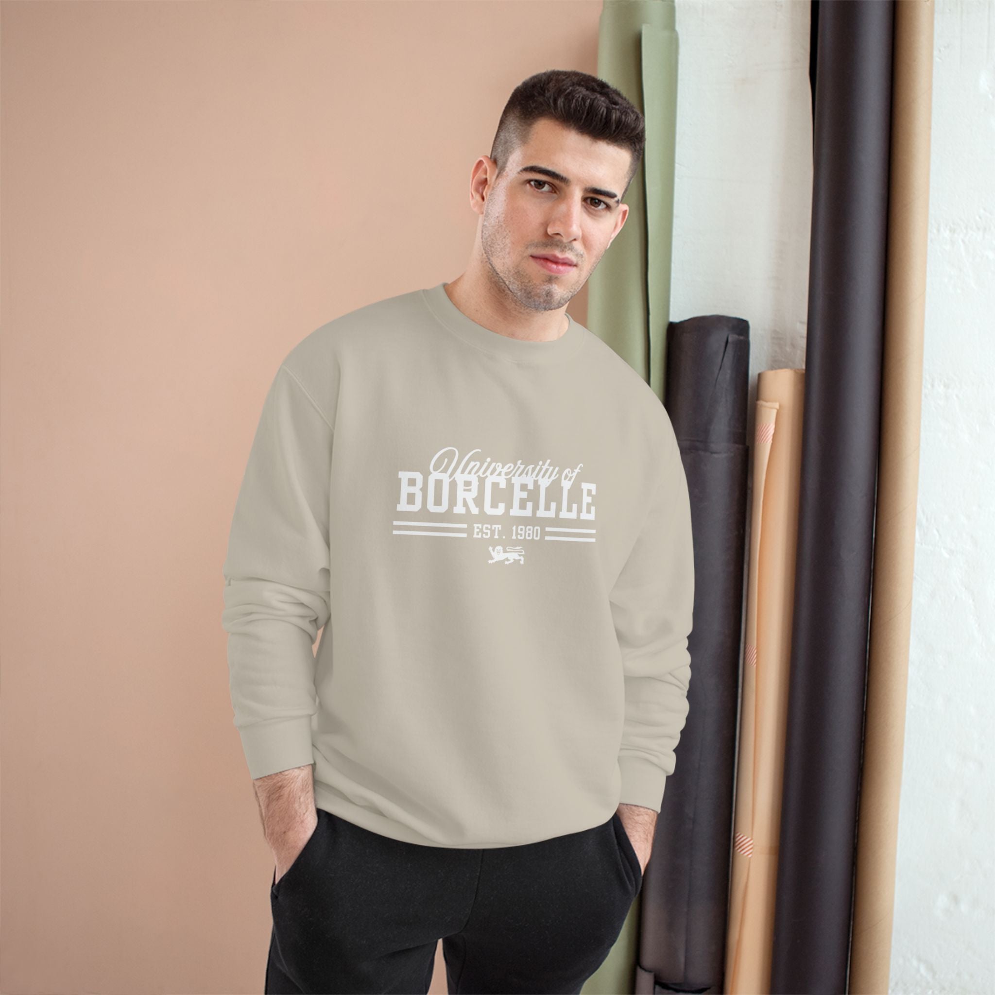 Man wearing a beige sweatshirt with 'University of Borcelle' text, standing against a beige wall.