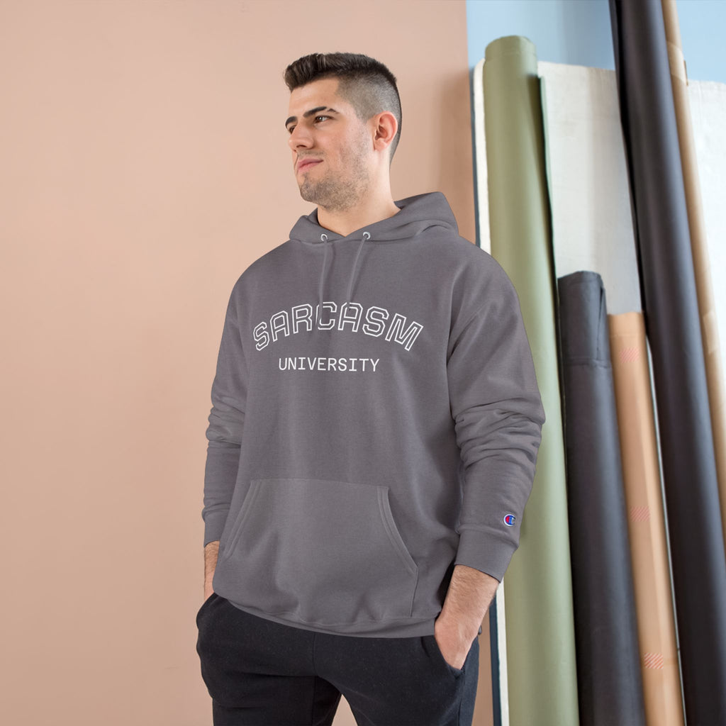 Man wearing a gray hoodie with 'SARCASM UNIVERSITY' text, standing against a beige wall.