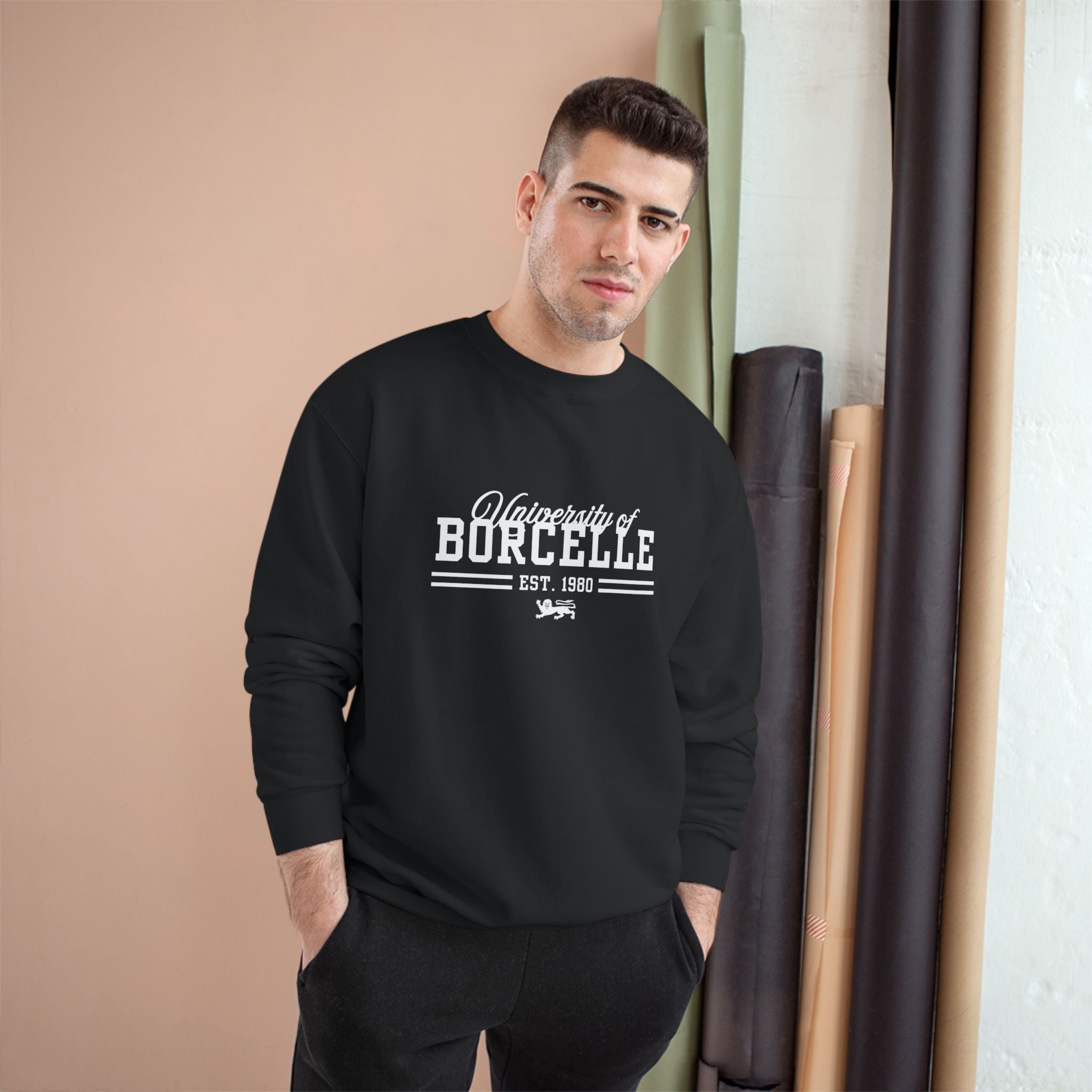 Man wearing a black sweatshirt with 'University of Burcelle' text, standing against a beige wall.